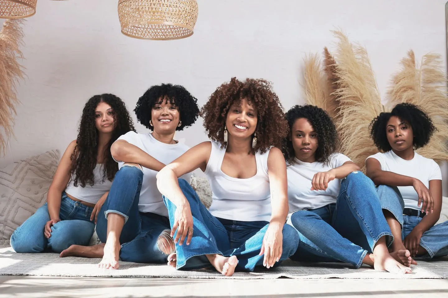 Cinq clientes aux cheveux bouclés, frisés et crépus assises ensemble dans un studio lumineux